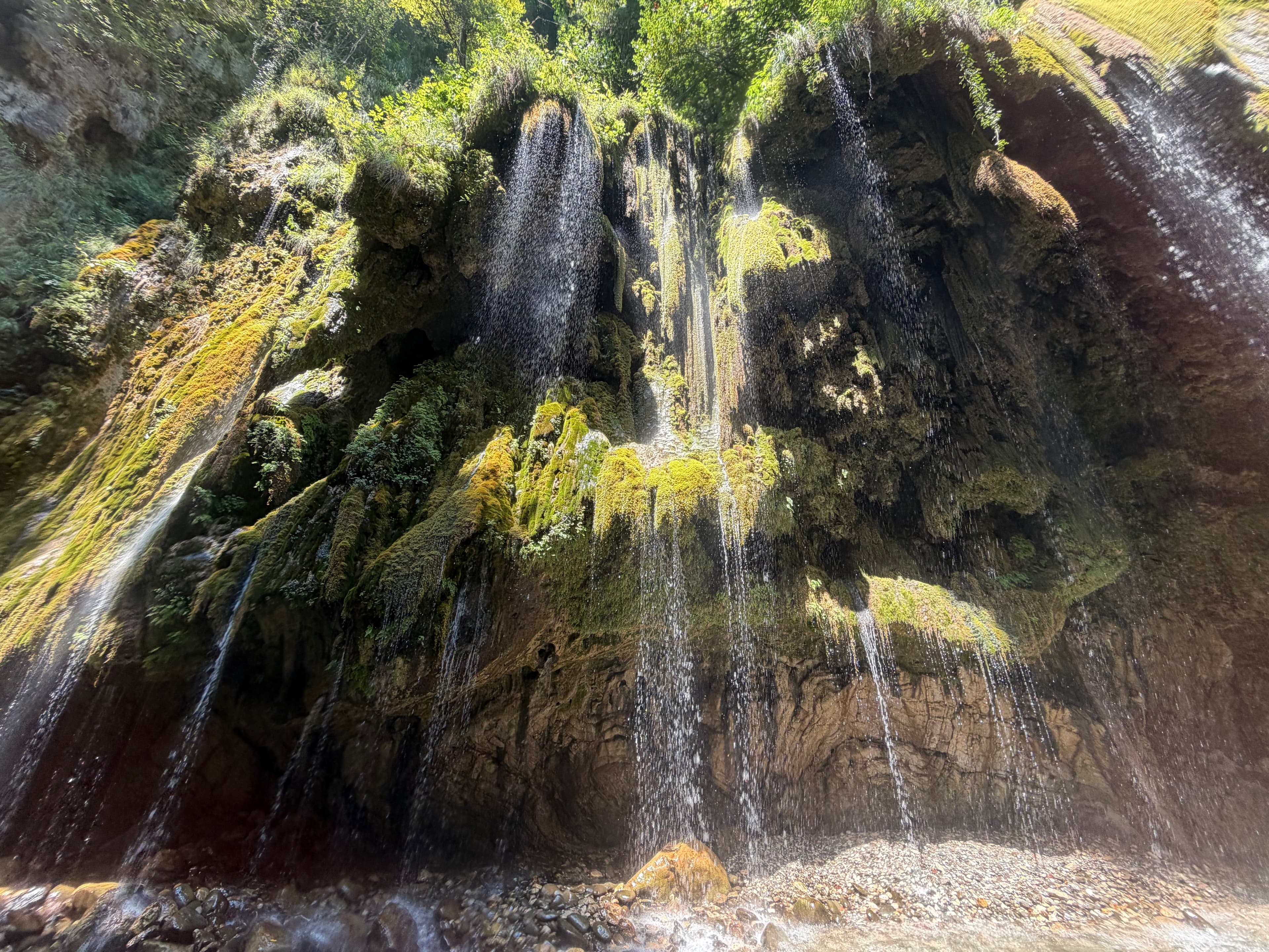 Panta Vrechei rock wall with dozens of small waterfalls dripping down moss-covered stone